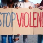 Mehrere Menschen halten ein Pappschild auf dem steht "Stop Violence"
