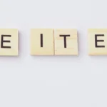 Holzplättchen mit Buchstaben bilden die englischen Wörter „TAKE IT EASY“ auf hellem Hintergrund.